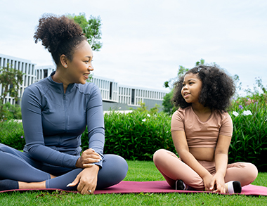 Young mother and daughter doing yoga together outside at home.