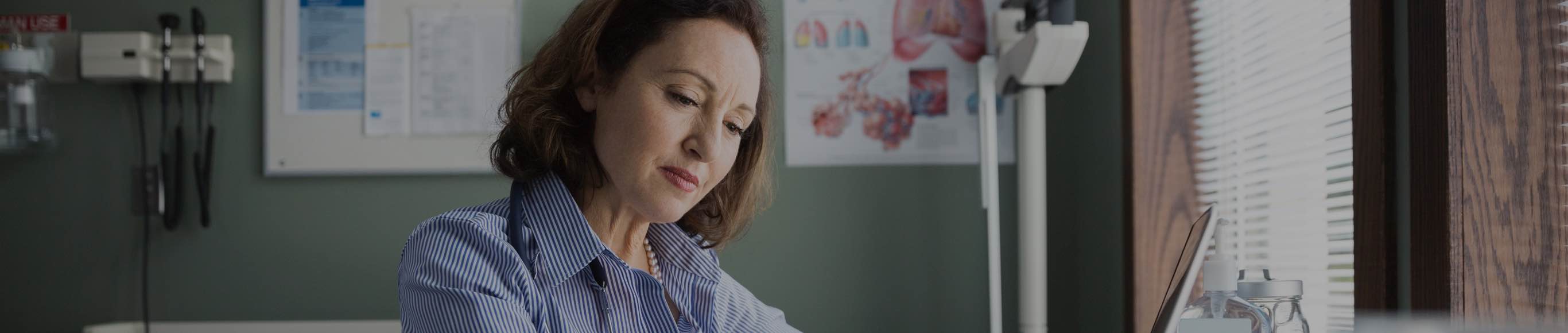 Woman looking down at laptop in doctor's office.