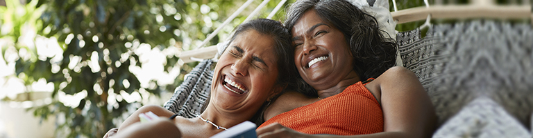 Cheerful young woman lying with happy mother on hammock outdoors