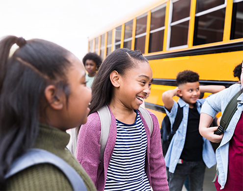 A young schoolgirl smiles cheerfully as she talks with friends in front of a school bus 